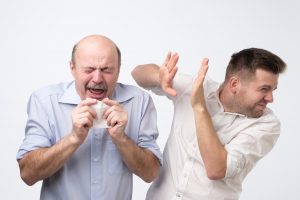 Older man sneezing in front of younger man